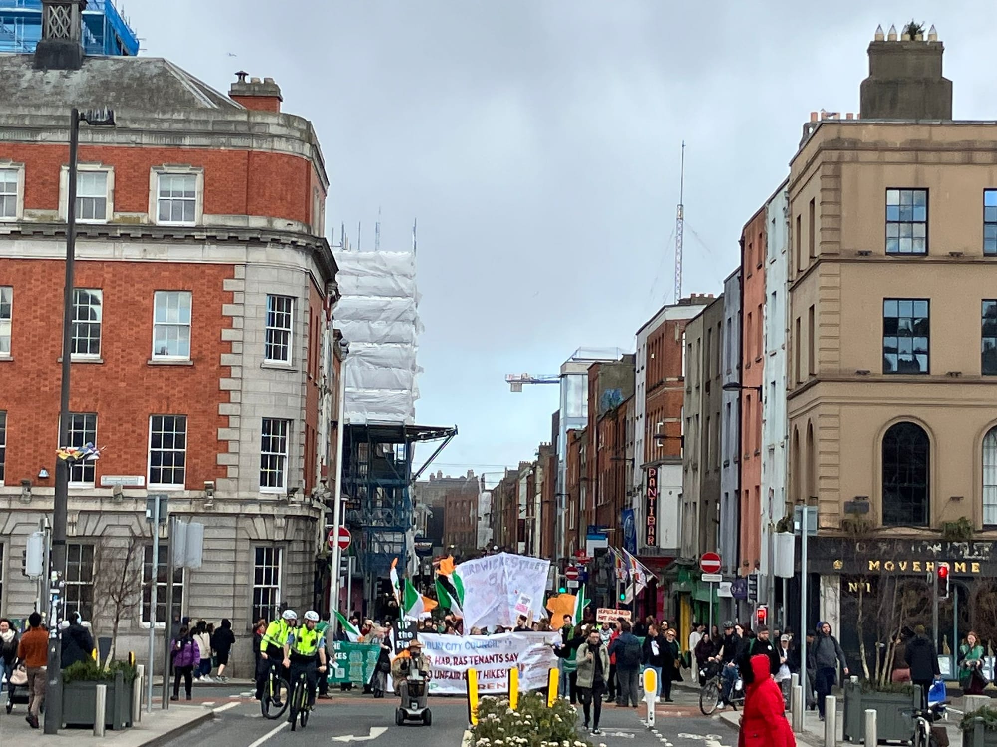 View of the march approaching Parliament Street bridge. Banners Irish Flags and Gardaí on bikes.