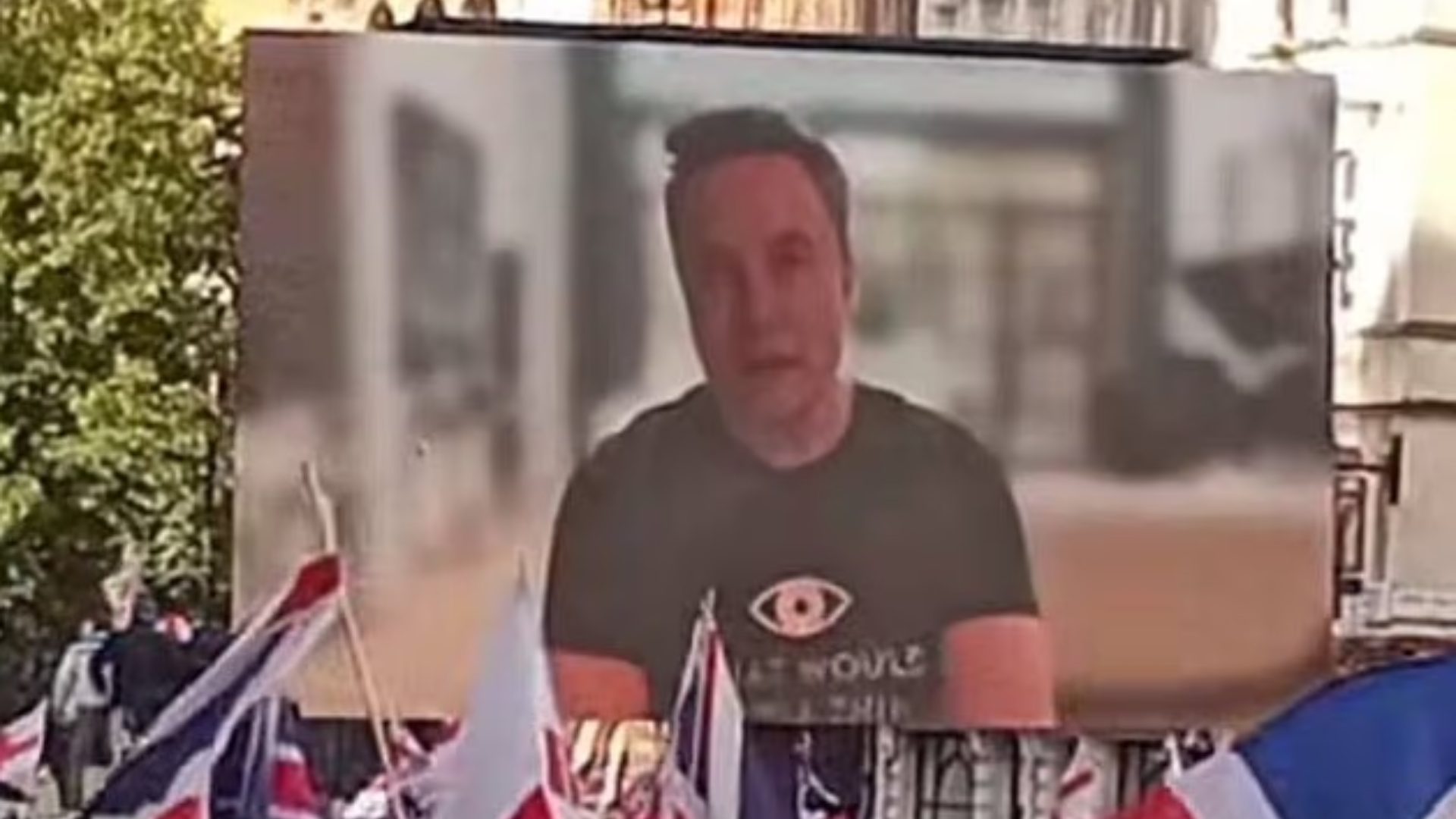 Elon Musk on screen at the anti-immigration rally in London. UK flags in foreground.