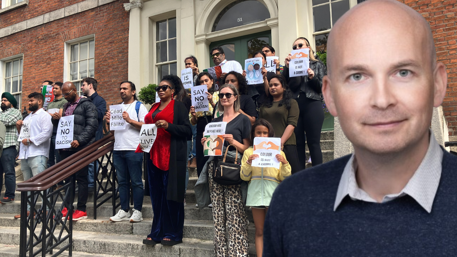 Paul Murphy in front of a photo of the August 2025 Demonstration at the Dept of Justice after a brutal racist attack in Dublin.