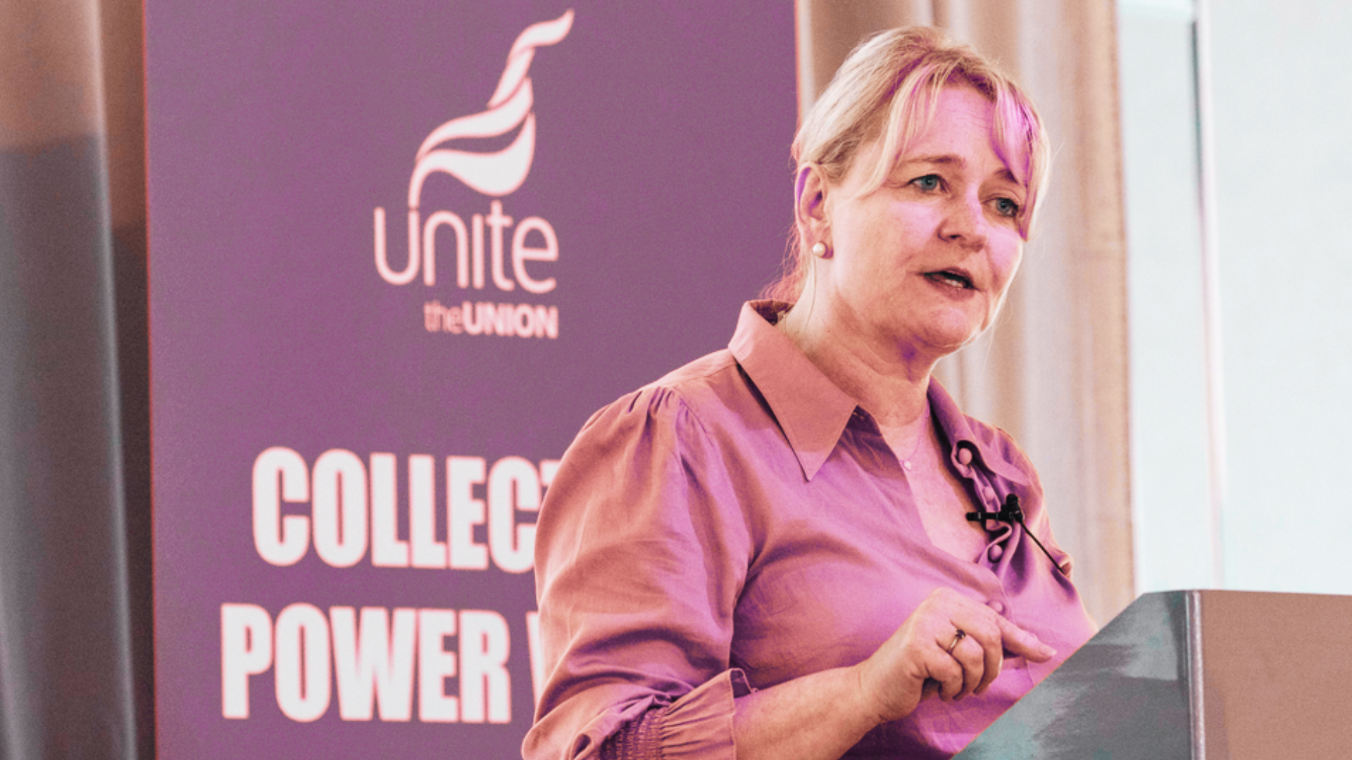 Incumbent General Secretary of Unite, Sharon Graham, standing at a lectern in front of a Unite the Union poster.