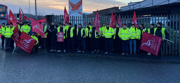 About 30 workers in hi-viz jackets holding Unite the union flags on strike in Belfast at an industrial park.