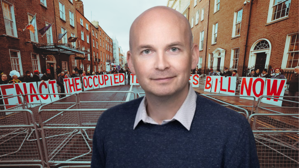 Paul Murphy in front of an image of protestors with giant single letter cards spelling out ENACT THE OCCUPIED TERRITORIES BILL NOW.